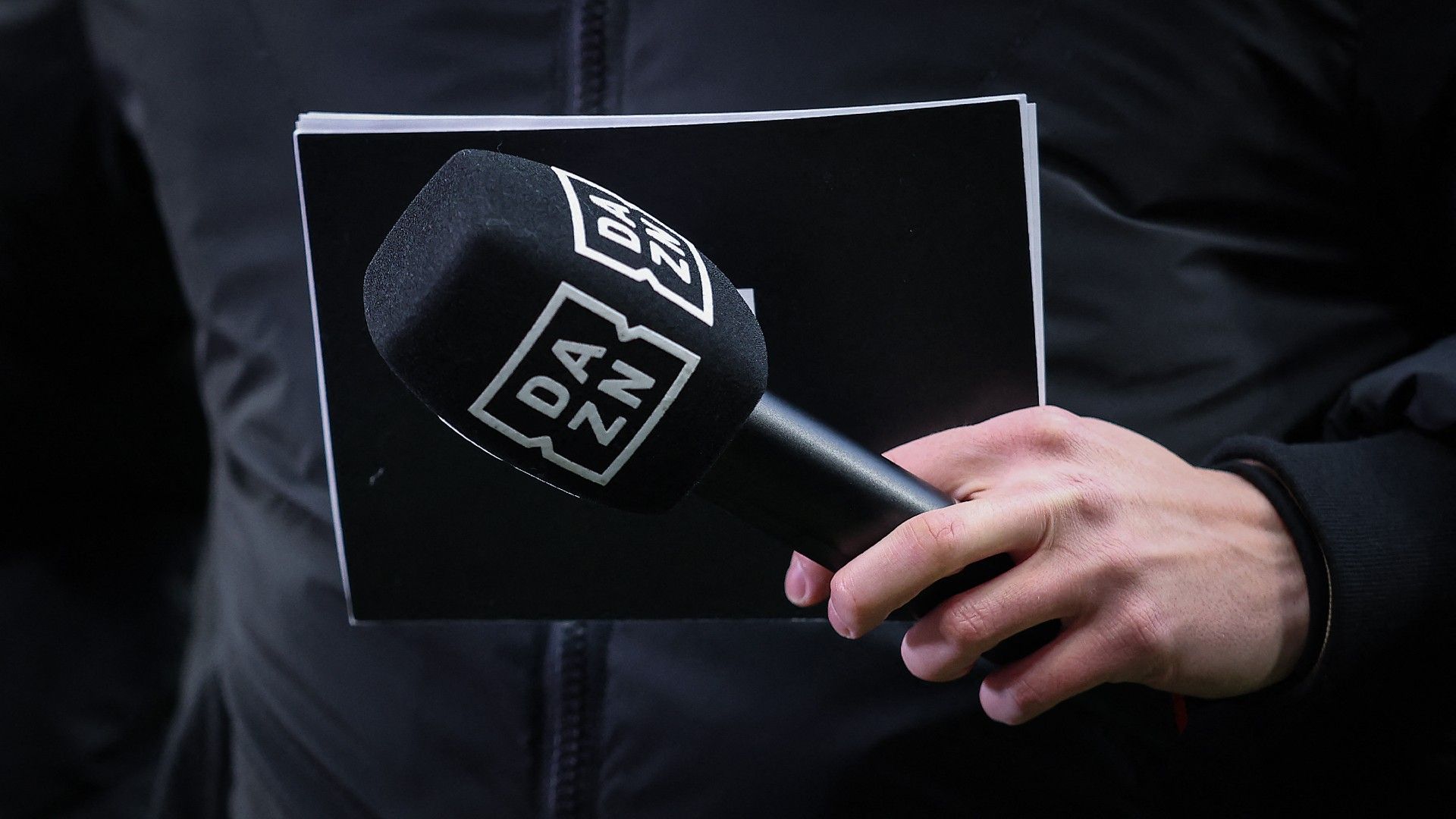 A journalist holds a microphone of British sports streaming and entertainment platform's DAZN