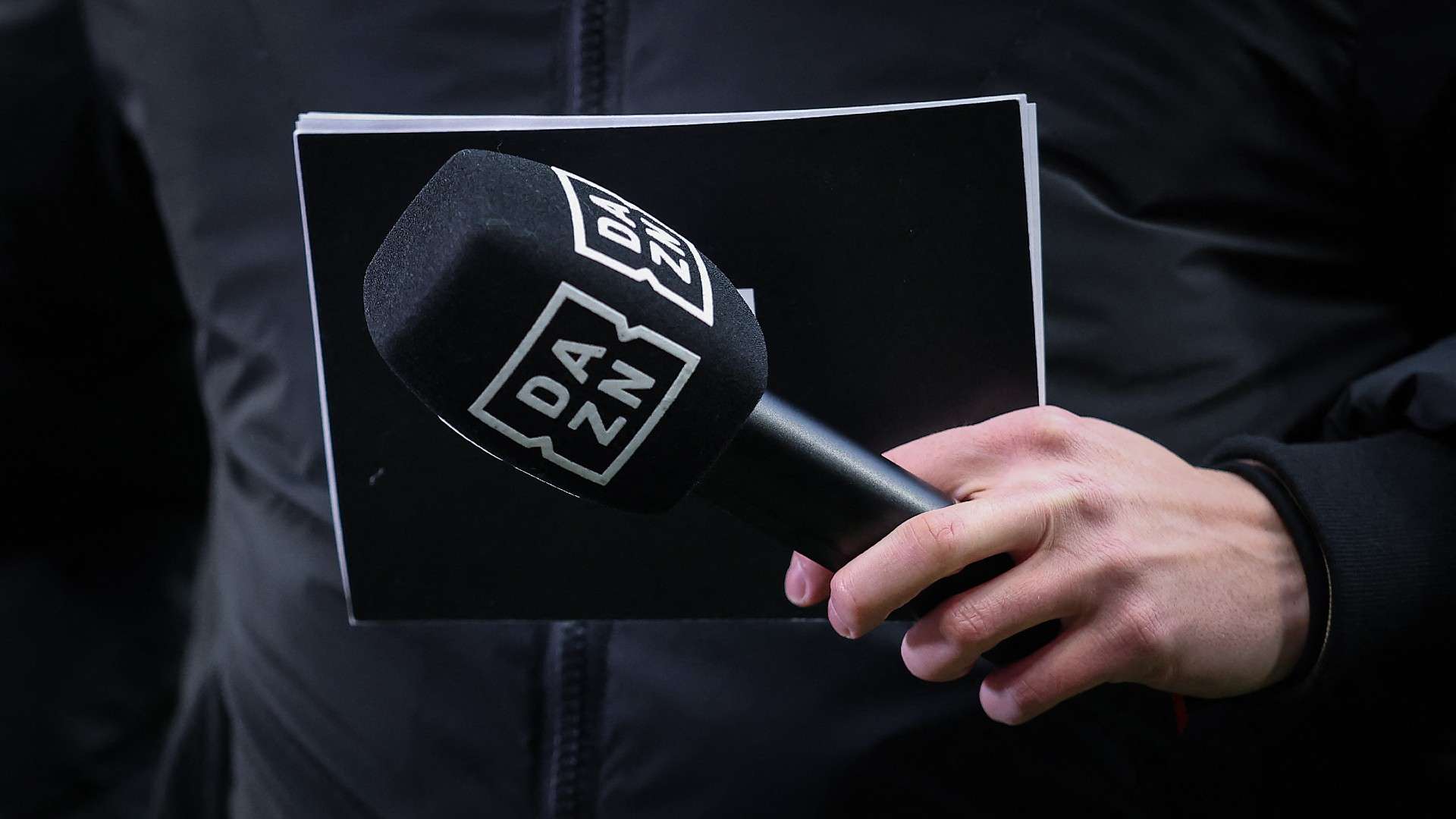 A journalist holds a microphone of British sports streaming and entertainment platform's DAZN