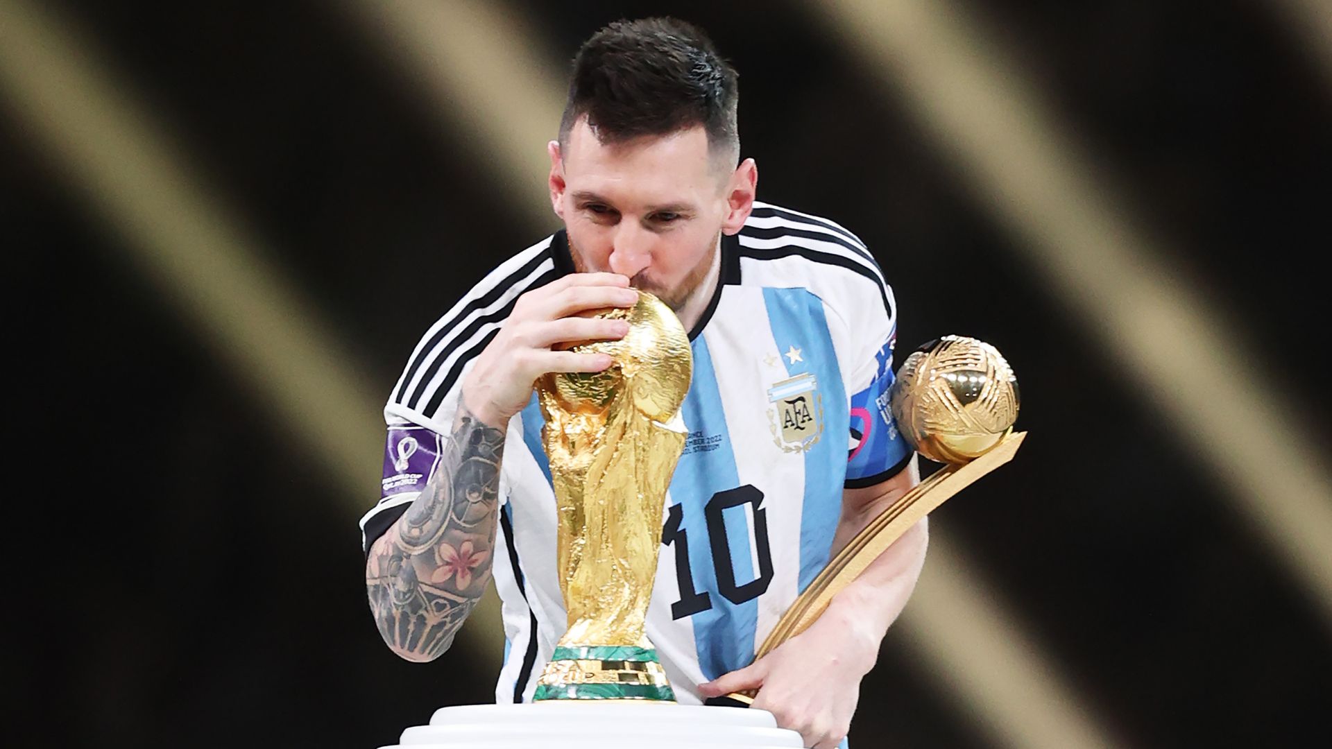 Lionel Messi of Argentina kisses the FIFA World Cup Qatar 2022 Winners' Trophy while holding the adidas Golden Boot award