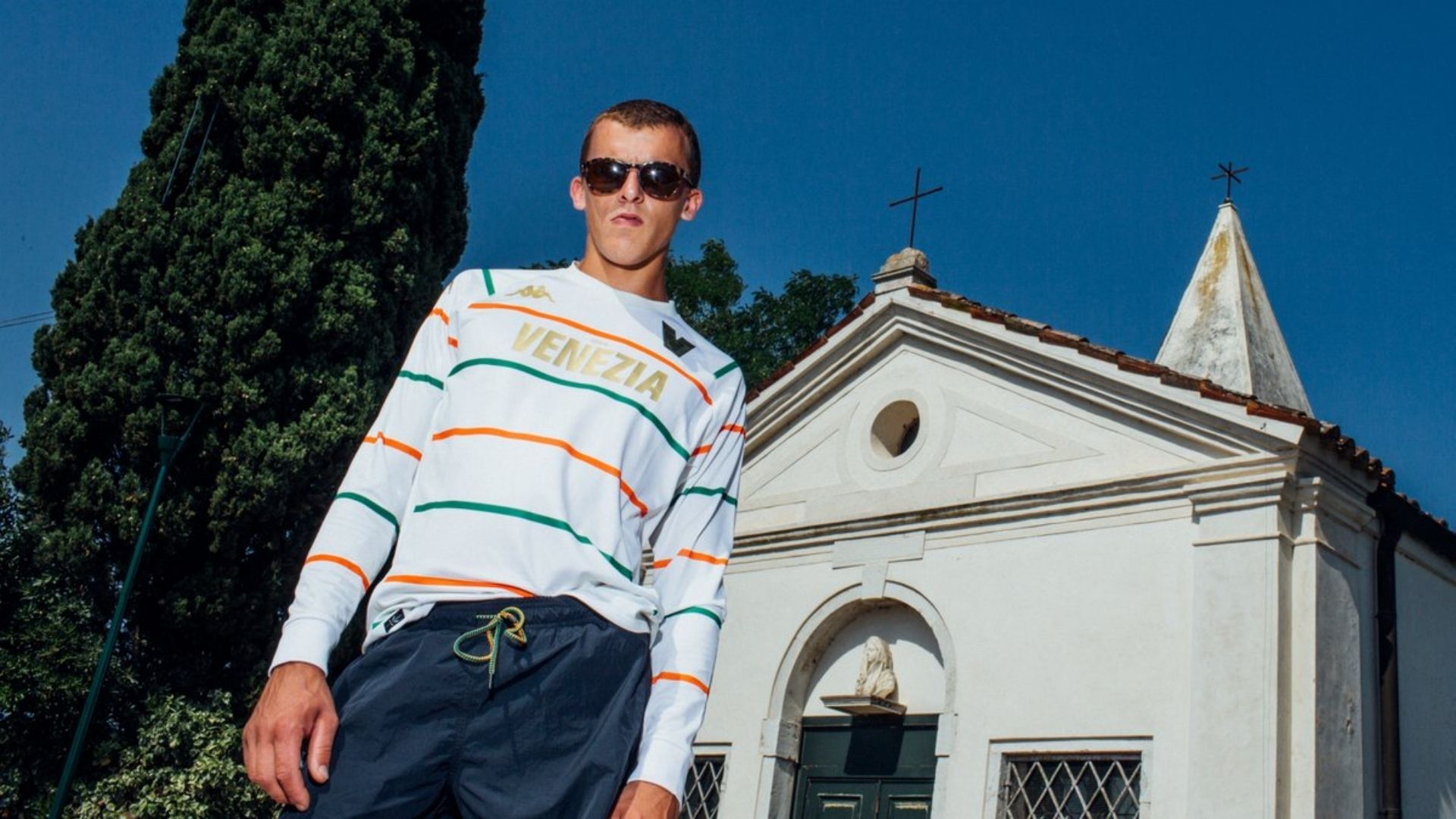 Dopo il successo riscosso dalla maglia home 22/23 - considerata da GQ e dagli altri principali media nazionali ed internazionali come una delle migliori maglie dell'anno, e che ha visto la sua versione a maniche lunghe andare sold out in poco più di 24 ore - il Venezia FC presenta la maglia da trasferta 22/23.  Mentre la maglia home, di colore nero intenso nastrata di sottili strisce arancioni e verdi, rimanda al linguaggio dell’alta moda, la maglia away, di colore crema chiaro e adornata di strisce arancioni e verdi più evidenti, ha un aspetto più fresco e sportivo. Dal colletto della maglia home si passa a un girocollo nella maglia away, e anche le decorazioni in oro vengono interpretate in una chiave diversa: la scritta Città di Venezia, che nel kit home si declina in un elegante carattere serif tradizionale, nella maglia da trasferta appare in un carattere sans-serif più moderno. Le due maglie - entrambe disegnate dal prestigioso studio Bureau Borsche e prodotte da Kappa, il technical partner del club - rispondono a filosofie diverse, ma sono complementari e collegate da un DNA comune. Non esprimono solo il medesimo approccio minimalista: una similitudine, infatti, si rileva anche nelle strisce arancioni e verdi che attraversano sia la maglia home che quella away, le quali sono, in entrambi i modelli, identiche linee di 10 mm.  L'approccio si rifà al tema della dualità presente nel lavoro del club, che cerca di fondere la tradizione e la modernità di Venezia, la sua dimensione internazionale e quella locale, così come la laguna e la terraferma.