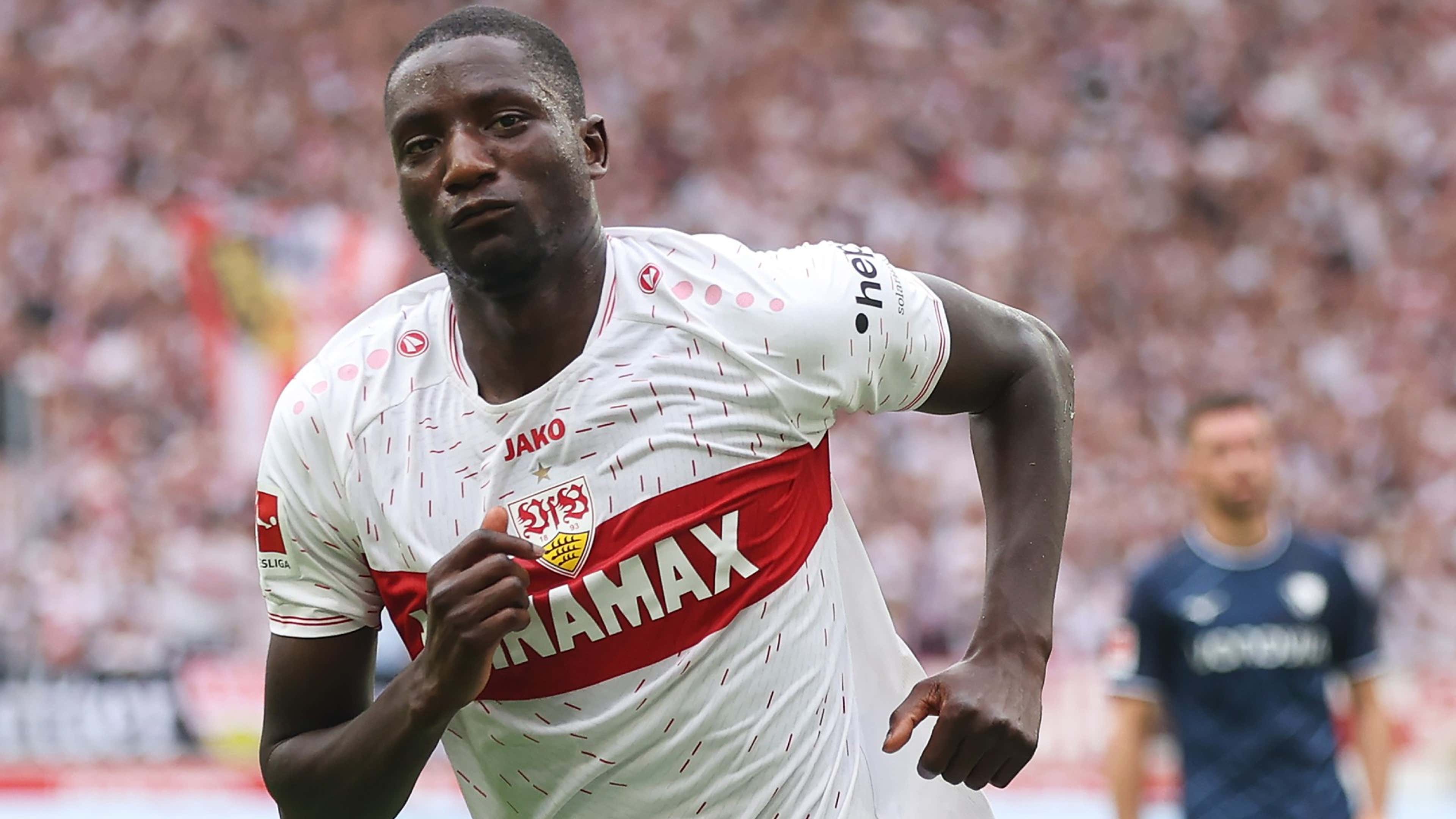  Serhou Guirassy, a professional football player, in a white and red jersey with the word 'JAMAX' on the front, is sprinting during a match.